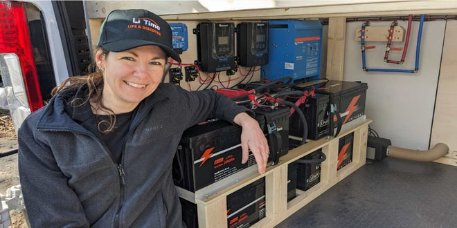 Mel of Home A Roam smiles next to their LiTime battery bank and electrical components in their campervan build