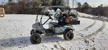 A camo golf cart sits in a snowy landscape, ready for winter use, featured in a litime lithium golf cart battery customer review