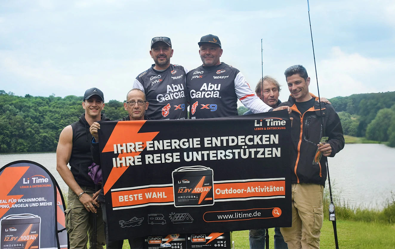 A group of participants from the Peche Fishing Game event hold up a large German-language LiTime banner by a lake