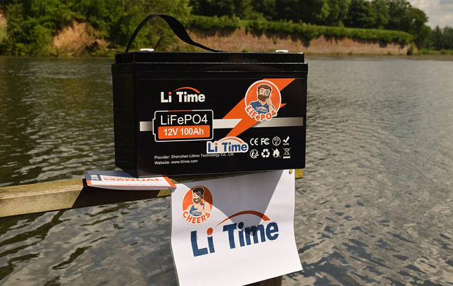 a LiTime 12V 100Ah battery sitting on a wooden dock with a lake in the background