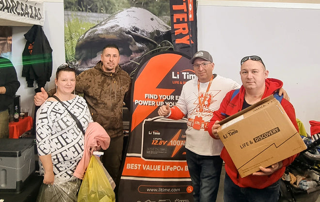A group of happy attendees pose together at the LiTime booth, with one man holding a large branded prize box