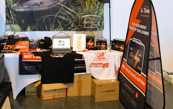 a product display at the LiTime expo booth, featuring various batteries, promotional t-shirts, and branded boxes