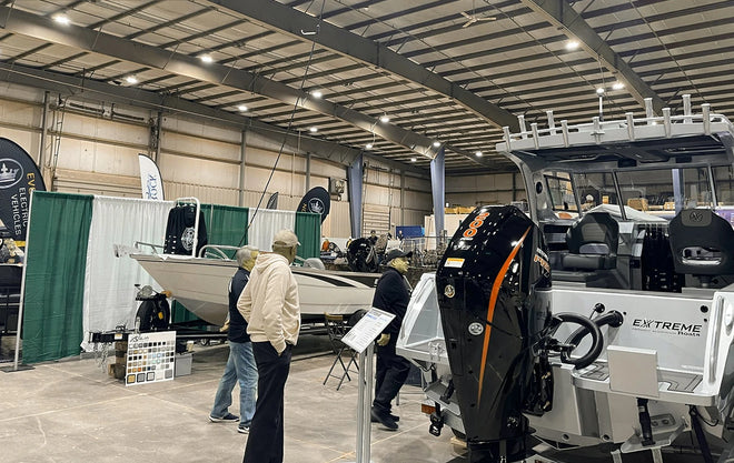 An indoor shot of the JDM Show, with several attendees viewing a display of fishing boats in an exhibition hall