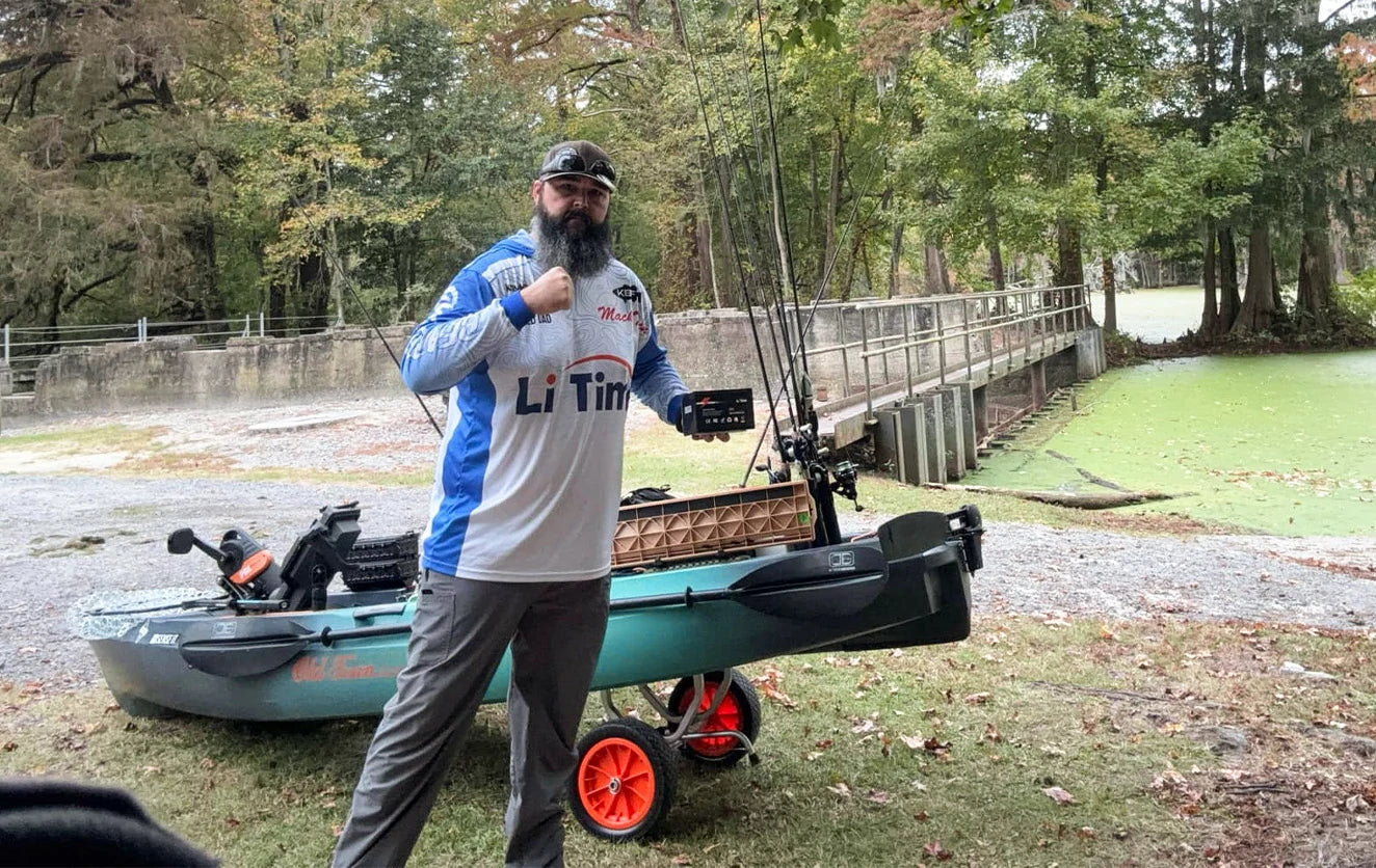 YouTuber Bearded Dad Fishing in his Li Time jersey, posing with his fully rigged fishing kayak by a boat launch