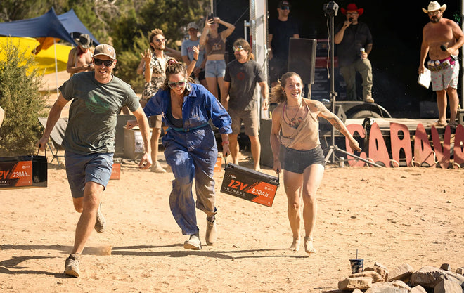 3 smiling competitors run towards the camera while carrying heavy LiTime batteries during a race at the Moonlanding event