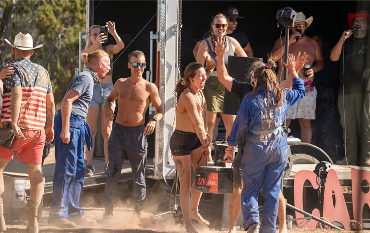 A crowd celebrates with the winner of a competition who is holding a large battery prize at the Moonlanding event