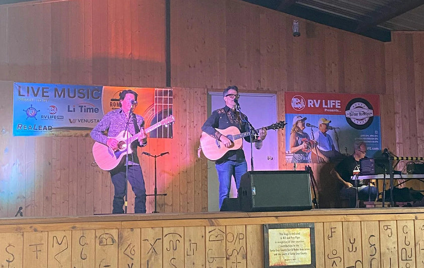 A band performs on stage at the Romp It Up Music Festival, in front of a sponsor banner featuring the LiTime logo