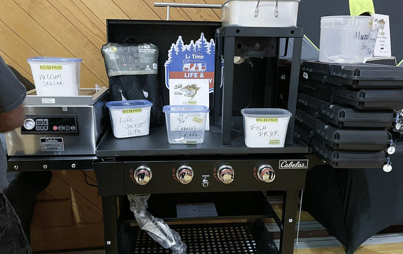 A table at the Walleye Fall Brawl, featuring a Cabela's cooking station, a vacuum sealer, and LiTime prizes
