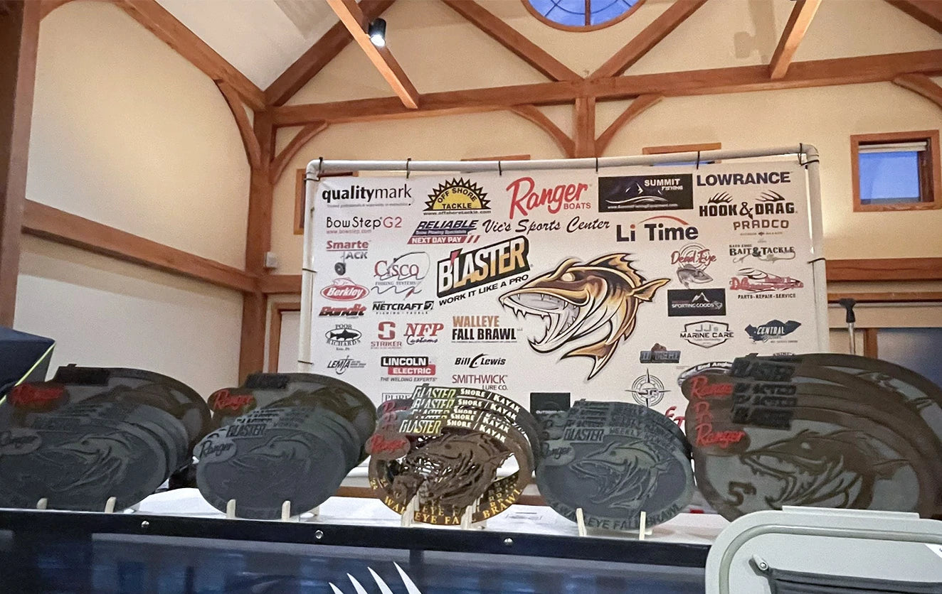 A close-up of the custom, fish-shaped metal trophies for the Walleye Fall Brawl, lined up before the sponsor wall