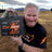 A man holds a LiTime 12.8V 100Ah battery outdoors, showcasing its features against a scenic desert backdrop