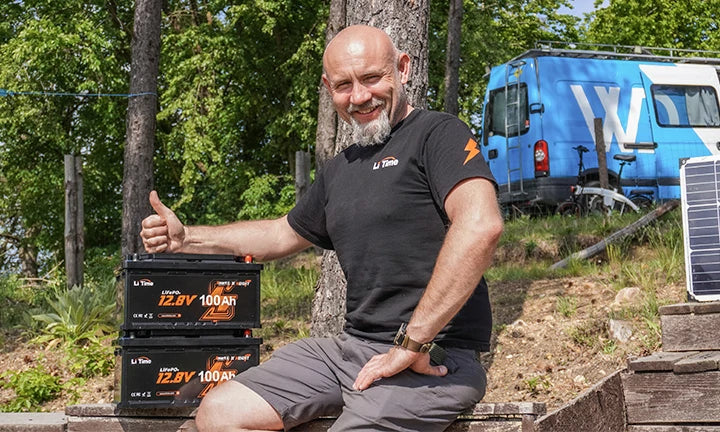 A man gives a thumbs up beside two LiTime 12V 100Ah batteries, highlighting their quality and reliability outdoors