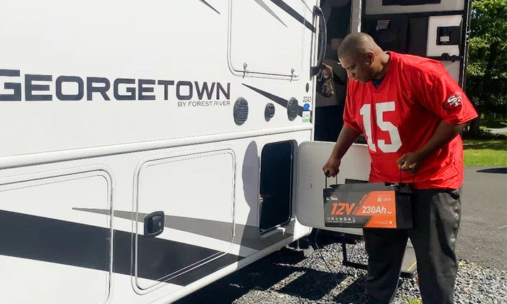 A man carries a LiTime 12V 230Ah battery towards an RV, showcasing its portability and use in camping