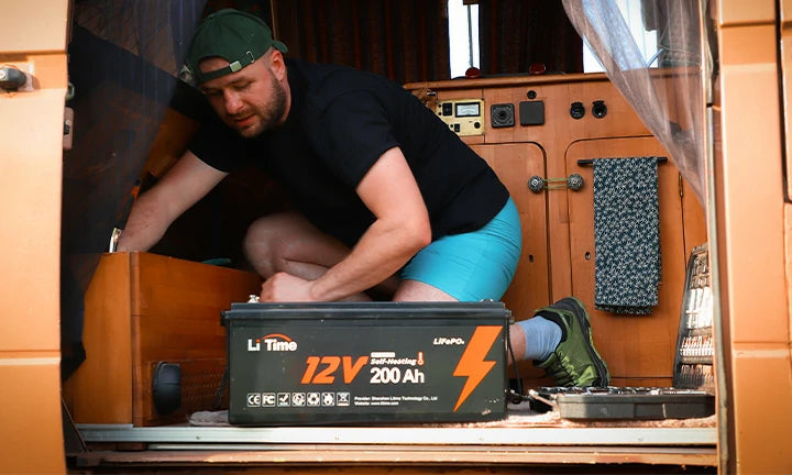a man in shorts organizes inside a van, with a LiTime 12V 200Ah lithium battery prominently placed nearby