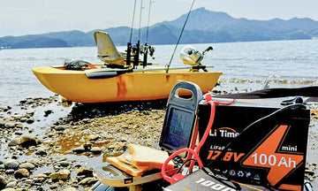 A LiTime mini battery sits on a rocky shore next to a yellow fishing kayak
