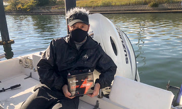 A fisherman wearing a face covering sits in a boat, holding a LiTime battery on his lap