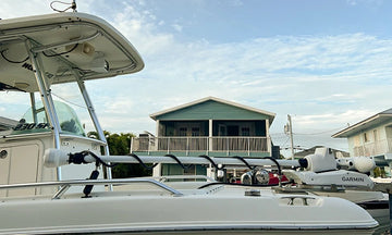 The bow and T-top of a white center console boat docked in the water in front of a house