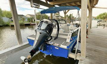 The stern of a blue and white boat with an outboard motor, docked under a covered slip.