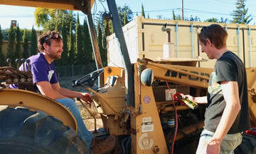 two men work on a tractor, one holding a tool, showcasing teamwork in maintenance for a litime lithium golf cart battery customer reviewv