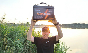  A delighted customer triumphantly holds up his new LiTime 100ah battery by a tranquil lake